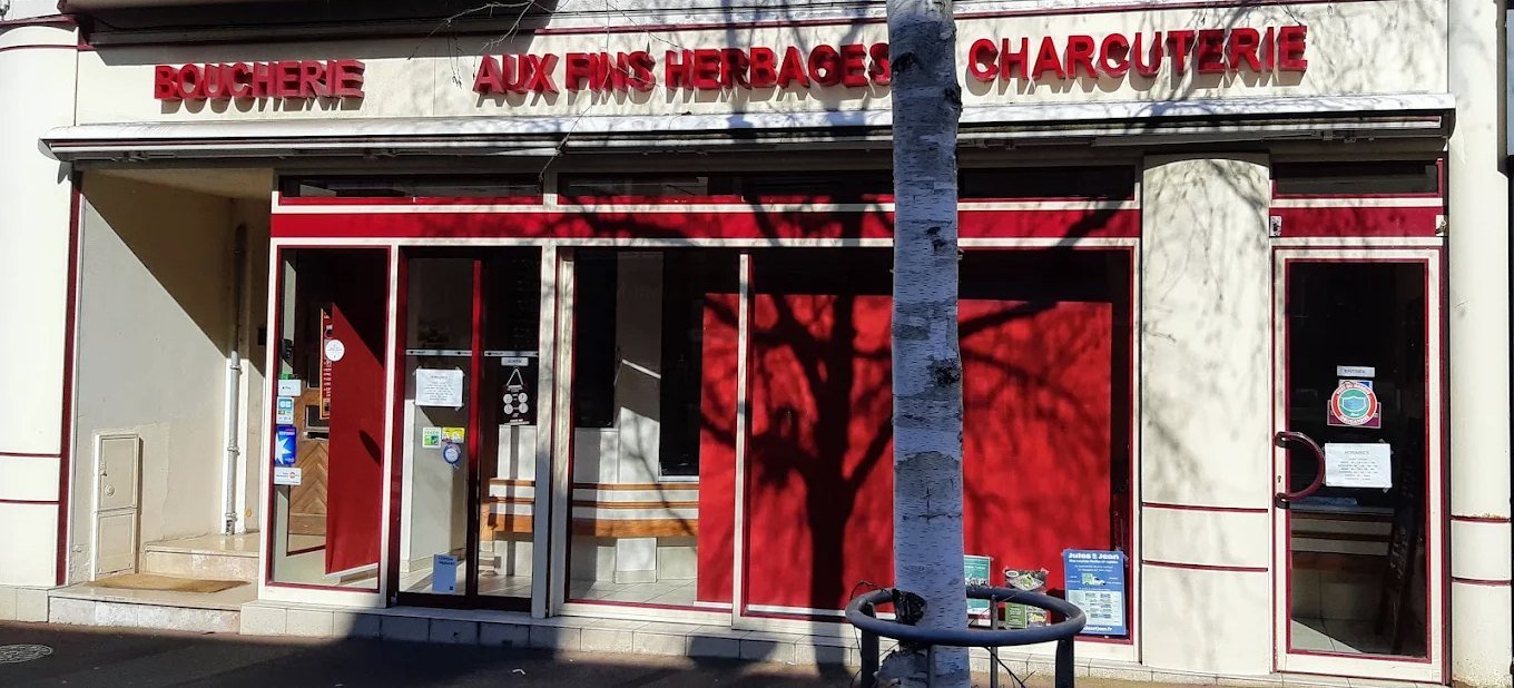 La devanture de la boutique : enseigne Aux Fins Herbages, vitrines rouges et porte d'entrée ouverte sur la rue